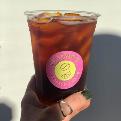 A hand holding an iced Americano in a plastic cup labeled with Graham's Coffee Parlor.