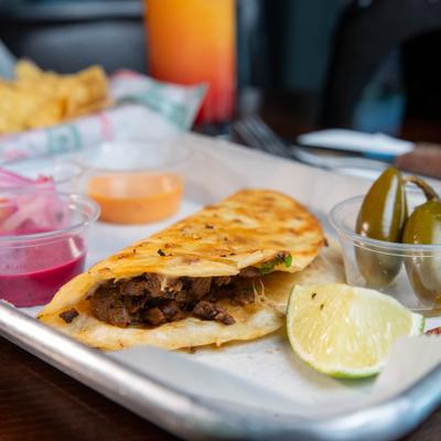 Street quesadilla served on a tray with sauces, pickled vegetables and a lime wedge.