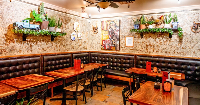 Cozy restaurant interior with wooden tables, cushioned booths, wall art, and decorative plants