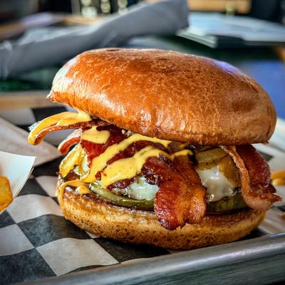 Bacon cheeseburger with melted cheese and pickles on a checkered tray.