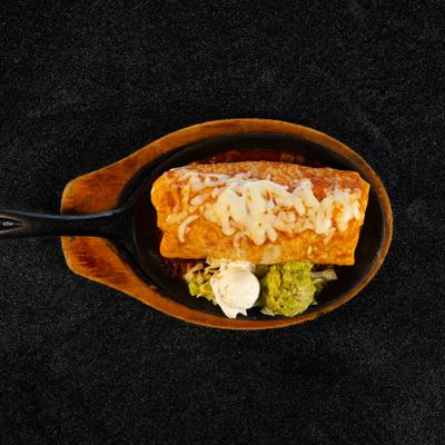 Fajita burrito served in a skillet with guacamole and sour cream.