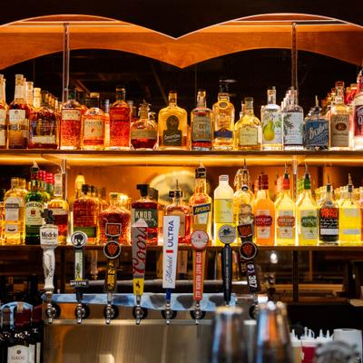 Backlit bar shelves filled with liquor bottles and beer taps in the foreground.