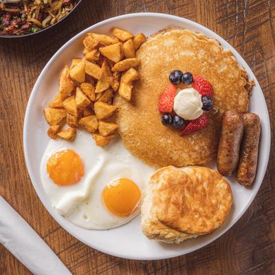 Plate with pancakes, roasted potatoes, two fried eggs, biscuit and sausage