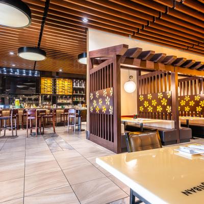 Restaurant interior with bar and dining section featuring wooden accents and decorative lighting.