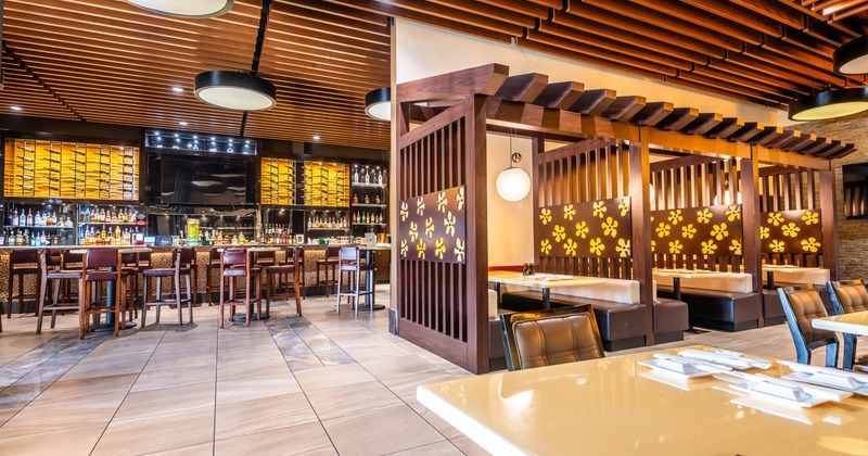 Restaurant interior with bar and dining section featuring wooden accents and decorative lighting