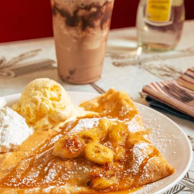 Crepe topped with banana slices and caramel sauce, served with ice cream and whipped cream.