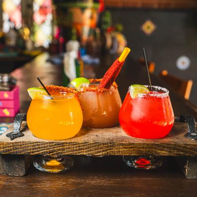 Cocktail flight featuring various flavors of margaritas served on a rustic wooden tray.