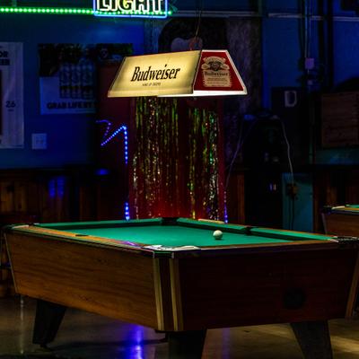 Pool table under vintage Budweiser light in a dark ba.