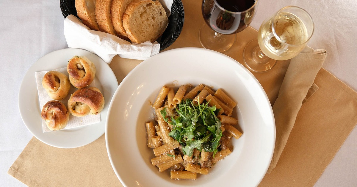 Rigatoni pasta with herbs served on a table with bread, garlic knots, and wine