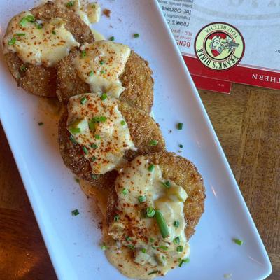 Fried green tomatoes topped with creamy sauce and green garnish on a  plate.