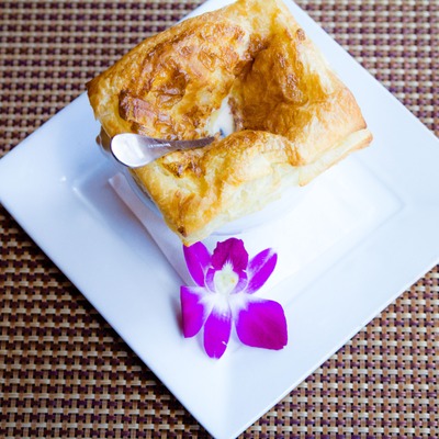 Golden pastry over soup on a white plate with orchid.