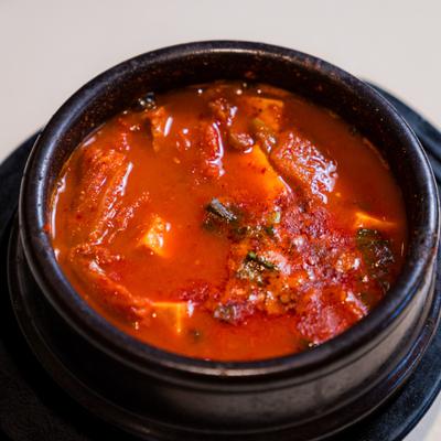 Spicy stew with tofu and vegetables in a dark pot.