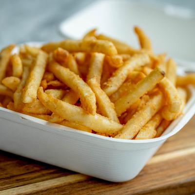 French fries in white container on a wooden table.