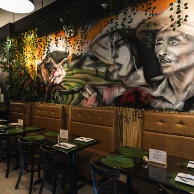 Interior, dining tables by a wall with mural art and hanging greenery.