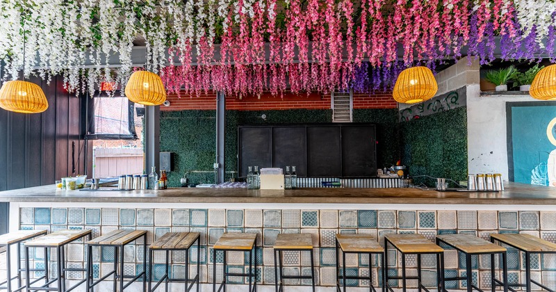 Tiled bar with stools, woven pendant lights, and colorful flowers hanging from the ceiling