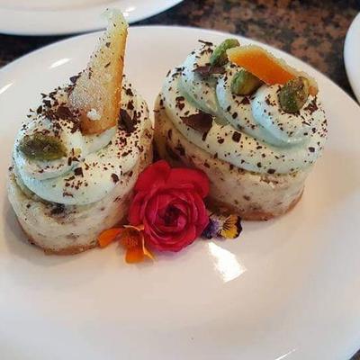 Two elegant dessert cups on a white plate, topped with cream, chocolate shavings, and fruit slices.
