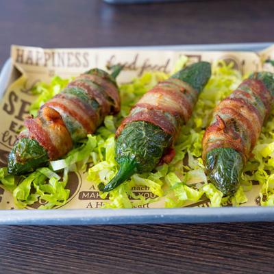 Bacon-wrapped jalapenos with shredded lettuce on a tray.