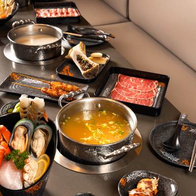 Hot pot dining spread with simmering broth, sliced beef, seafood, skewers, and assorted side dishes.