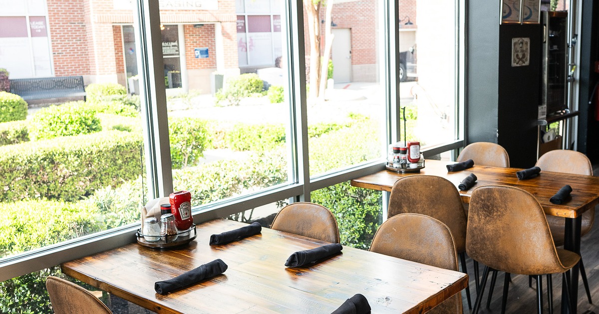 Dining tables set for four guests along windows