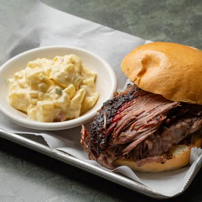 Sliced brisket sandwich on a bun served with potato salad side.