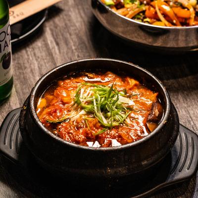 Korean kimchi stew in a traditional earthenware pot, garnished with green onions.