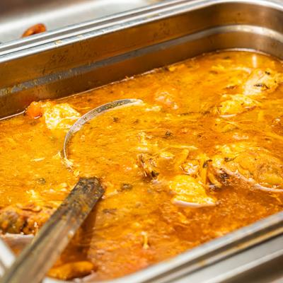 Chicken curry in a metal tray with a ladle.