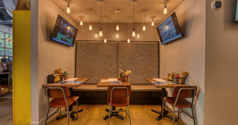 A restaurant booth - hanging light bulbs and two TVs, featuring wooden tables and chairs.