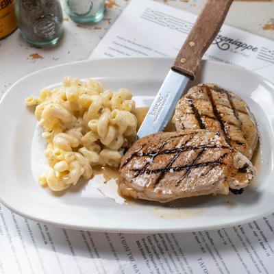 Grilled pork chop served with macaroni and cheese on a white plate.