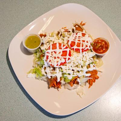 Tacos Dorados topped with lettuce, queso fresco, tomato and sour cream.