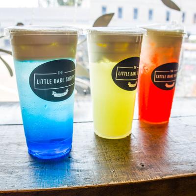 Three colorful layered beverages in clear, branded plastic cups.