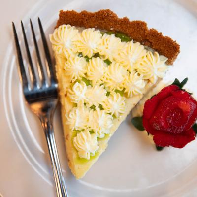 A slice of key lime pie on a white plate, garnished with a strawberry carved like a rose.