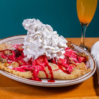 Crepe topped with whipped cream and strawberry sauce, served with a mimosa drink.