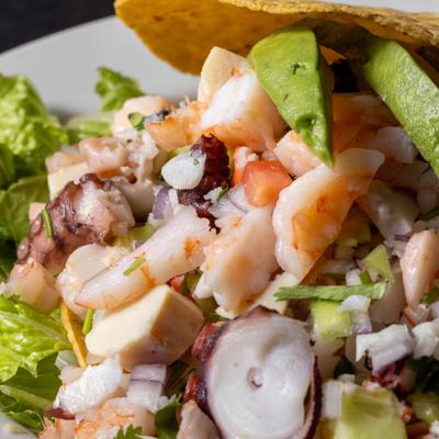 Tostada Mixto with raw seafood, avocado slices and fried corn tortilla, closeup.