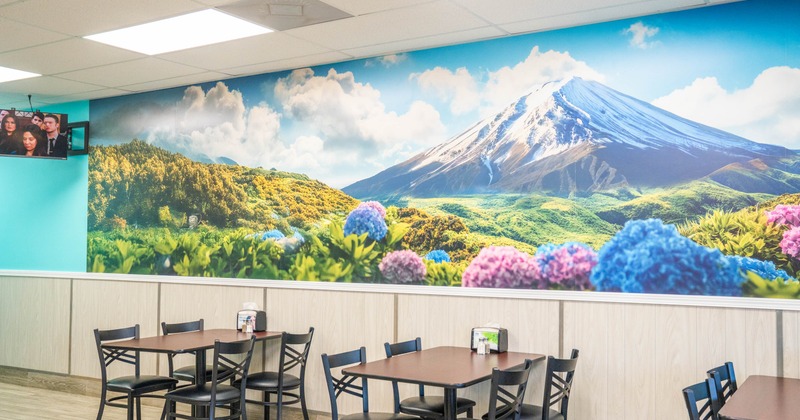 Interior, tables and chairs, a mural of a mountain landscape, and a TV on the wall.