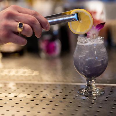 Bartender garnishes a glass of cocktail with an orange wheel.