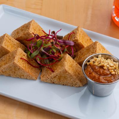 Fried Crispy Tofu garnished with microgreens and served with peanut dipping sauce.