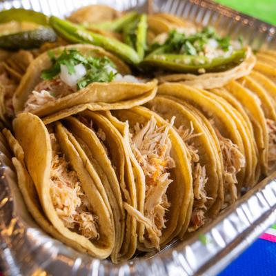 Shredded chicken tacos served in aluminum catering tray, close-up.