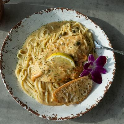 Creamy chicken pasta with lemon, capers, garlic bread, and a purple flower.