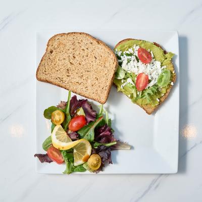 Sandwich with guacamole, arugula, feta, and grape tomatoes.