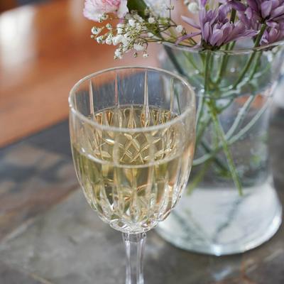 A white wine in a crystal glass next to a vase of flowers.