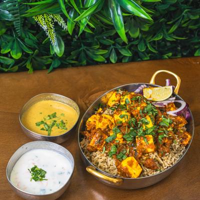 Paneer masala over spiced rice with raita and yellow curry on the side.