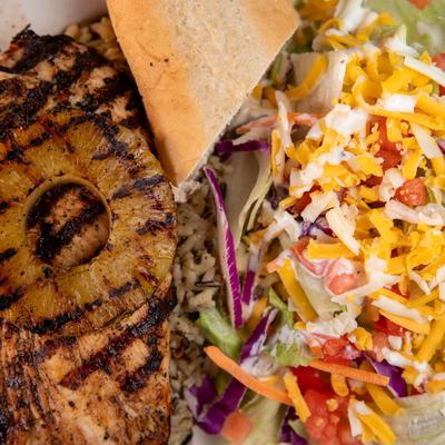 Grilled chicken with grilled pineapple slices, bread, and a salad, top view.