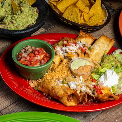 Crispy Yucatan Flautas, rice, lettuce, sour cream, beans, and a sauce on a red plate.