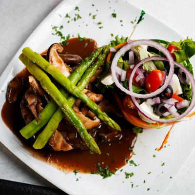 Steak topped with brown gravy, mushrooms, and asparagus, served with a side salad.