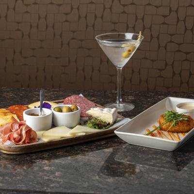A charcuterie board, martini, and crab cake on a table.