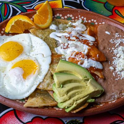 Chilaquiles plate with fried eggs. avocado, refried beans, and orange slices.