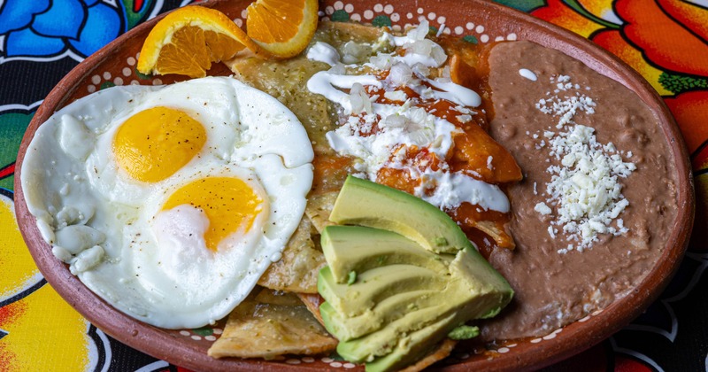 Chilaquiles plate with fried eggs, refried beans, avocado, and orange slices
