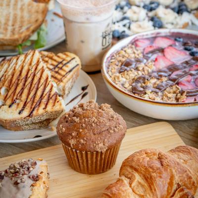 A vibrant spread of sandwiches, an iced coffee, an acai bowl, and pastries.