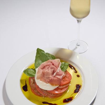 Burrata and prosciutto appetizer accompanied by a glass of sparkling wine.