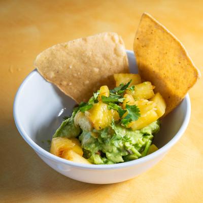 A serving of guacamole topped with diced pineapple and cilantro, served with chips.